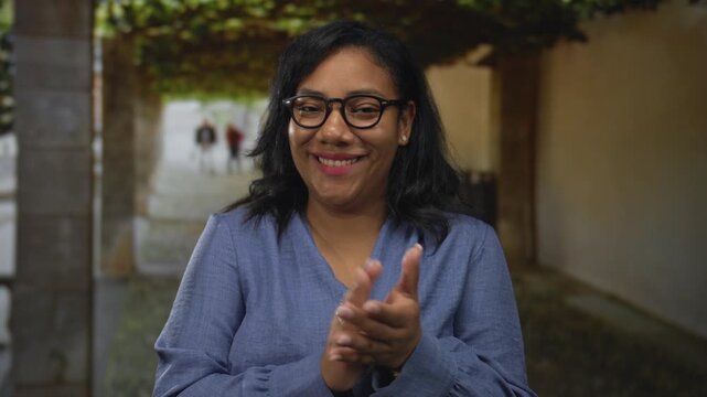 Woman clapping bare hands in building corridor lined with climbing vines and stone pillars; celebration.
