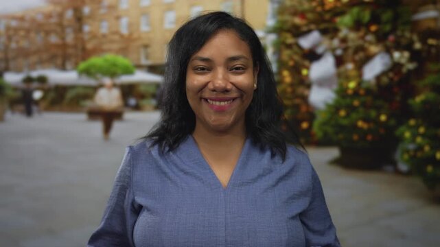 African american woman in blue blouse holds eyeglasses and smiles on city street; confidence clarity.