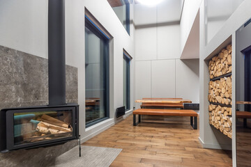 Fototapeta premium The interior of a country house in high-tech style. White decor with elements of black. A modern oven with a glass heat-resistant door. A place to store firewood.