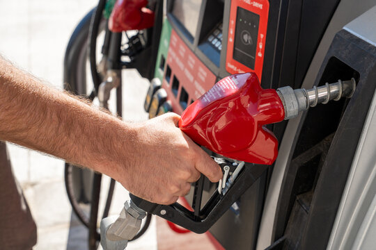 Close up of male hand holding fuel pump nozzle at gas station, concept of gasoline shortage, rising fuel prices and transportation energy, horizontal photo