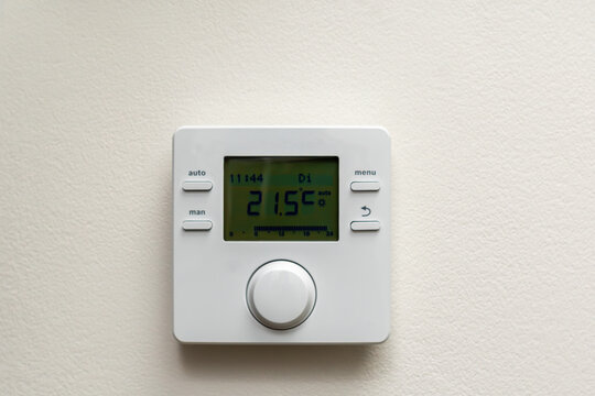 Modern white wall-mounted digital room thermostat with LCD display showing temperature for home heating control.