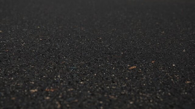 Slow motion video of the fresh asphalt surface in Siska, Ljubljana, a base of compacted grey aggregate and a thick, fresh layer of black asphalt.