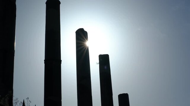 Silhouetted columns of ancient roman ruins against bright sun. Majestic ancient roman columns standing in silhouette against a bright, glaring sun, creating a dramatic lens flare effect