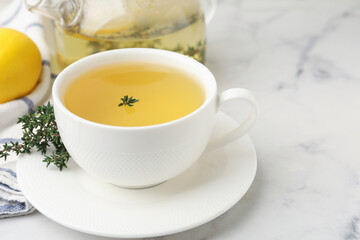 Fresh thyme tea in cup on white marble table, closeup. Space for text
