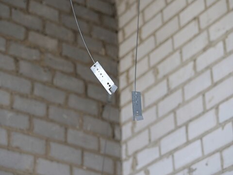 close up of metal ceiling hangers or suspension wires for drywall grid, interior construction site 
with white and grey brick walls in background, metal brackets hanging from ceiling wires