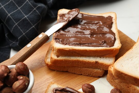 Toasts with chocolate paste, hazelnuts and knife on table, closeup