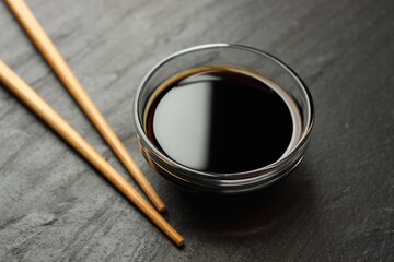 Soy sauce in bowl and chopsticks on black table, closeup