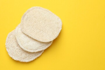 Natural loofah sponges on yellow background, flat lay. Space for text