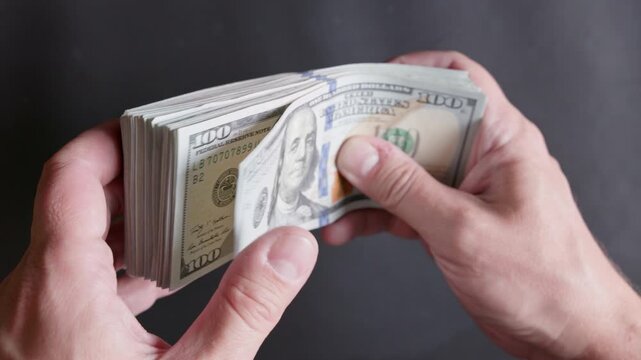Hands grasp a large stack of banknotes in a dimly lit studio. The scene exudes feelings of wealth, financial success, and abundance.