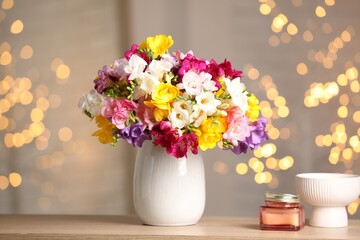 Fototapeta premium Beautiful freesia flowers in vase and candle on wooden table indoors. Bokeh effect