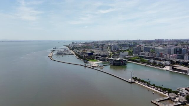 Aerial drone video slowly pushing in over the Tagus River towards the Lisbon Oceanarium and marina in the modern Parque das Nacoes district, showcasing the city beautiful waterfront