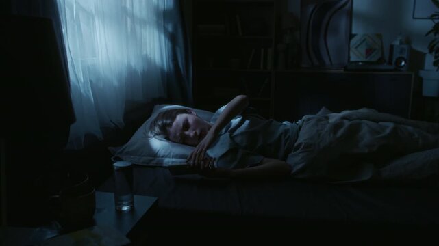 Young adult woman lying in bed waking up to incoming call on phone then turning signal off and going back to sleep during late night