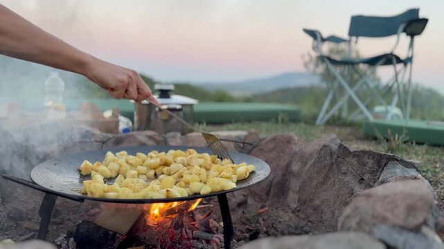 Authentic off-grid living: Hand stirring potatoes in a cast iron pan outdoors