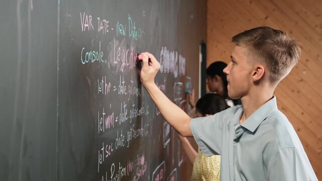 Site view of boy writing code on blackboard with diverse friend. Group of high school children using mind map to explain planing coding or programming system in STEM technology class. Edification