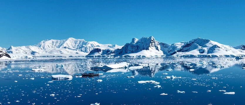 A small sailboat navigating through calm blue waters filled with icebergs and surrounded by snow-capped mountains