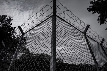 Chain-link fence topped with barbed wire against a cloudy sky, security protection concept