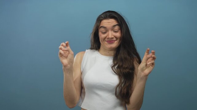 Hispanic woman holding fingers in air quotes with raised eyebrows and playful grin in a blue studio; sarcasm irony.