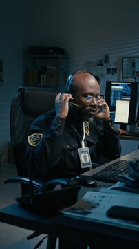 Vertical shot of African American man as police officer picking up phone and making calls in control room during night shift