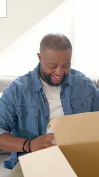 Vertical video: Receiving shipping box, man in denim shirt opening box on couch, inspecting product