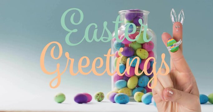 Hand entering, lifting bunny-eared fingertip toward jar, showing pastel eggs under Easter Greetings