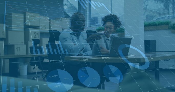 Pointing two colleagues in business attire reviewing laptop data at meeting table, with charts