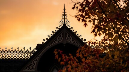Obraz premium Ornate Victorian house roofline with decorative gingerbread trim silhouetted against golden sunset sky creating atmospheric architectural scene.