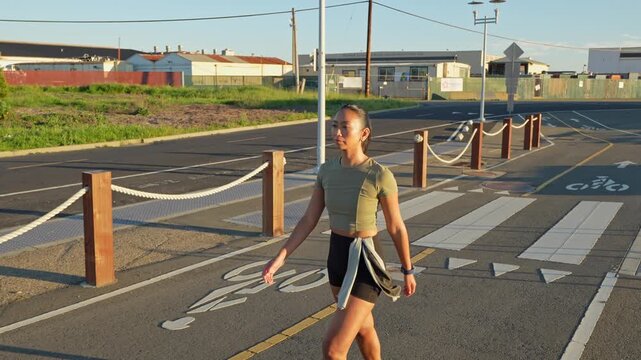 Young asian woman wearing earbuds running along an urban path in Alameda, California, during a sunny afternoon, embodying an active and healthy lifestyle through regular physical exercise