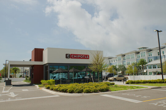 Chipotle Restaurant Exterior With Outdoor Patio Seating and Umbrellas in Urban Shopping Center Editorial Use Only March 9, 2026, St. Petersburg,FL USA. Large glass windows and red signage, parked cars