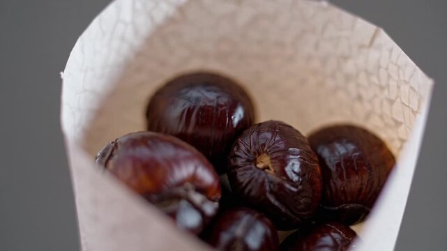 Close up of roasted chestnuts inside paper cone highlighting texture detail and natural food surface with minimal composition and focus on simplicity.