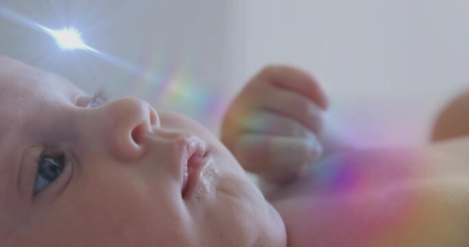 Baby girl lying on back, tracking rainbow prism light sweeping by, blinking for health demo