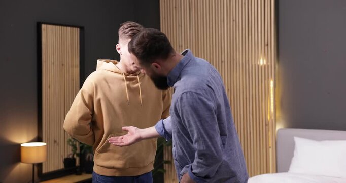 Alcohol addiction. Drunk man hiding bottle of beer from his friend indoors
