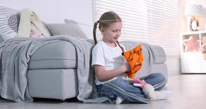 Cute girl playing with puppets on sofa at home