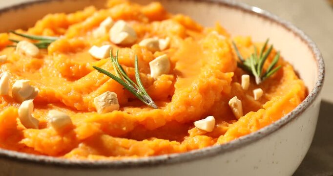 Delicious mashed sweet potato with cheese and rosemary in bowl on table, spinning. Closeup view