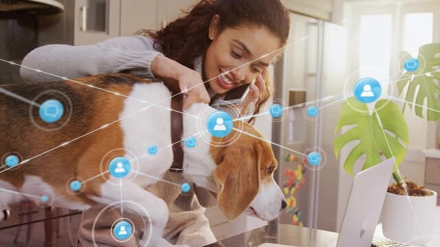 Vertical video: Answering call woman in sweater on phone at counter petting dog near laptop overlay