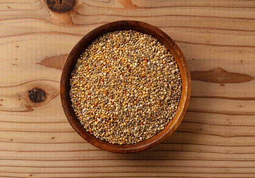 Top view of mixed bird seed in a wooden bowl on a wooden table