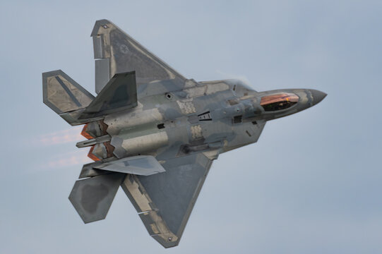 Lockheed Martin F-22 Raptor stealth fighter jet banking with afterburners against cloudy sky