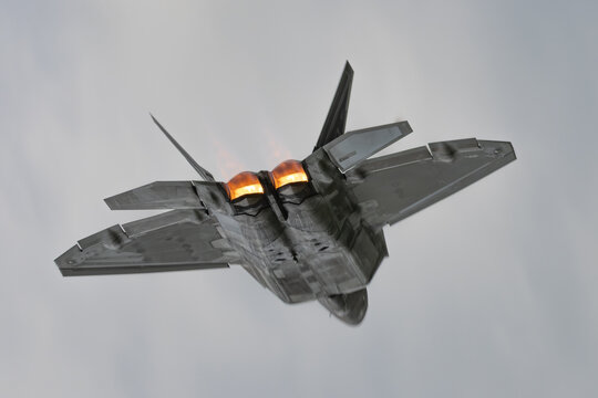 Lockheed Martin F-22 Raptor stealth fighter jet climbing with afterburners against gray sky