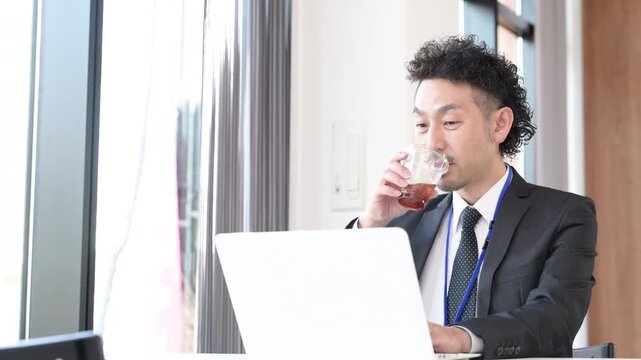 ノートパソコンを使い笑顔のビジネスマンの髭の男性　デスクで仕事をする動画　休憩でコーヒーを飲む