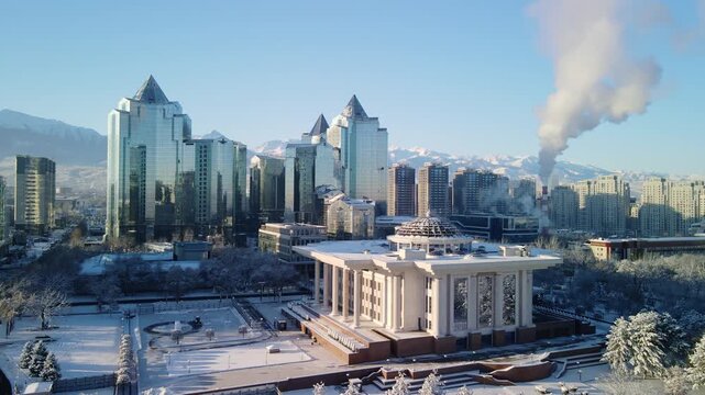 Aerial drone view of Almaty city after heavy snowfall. Winter panorama of Nurly Tau business center, snow-capped residential buildings and Trans-Ili Alatau mountains in Kazakhstan.