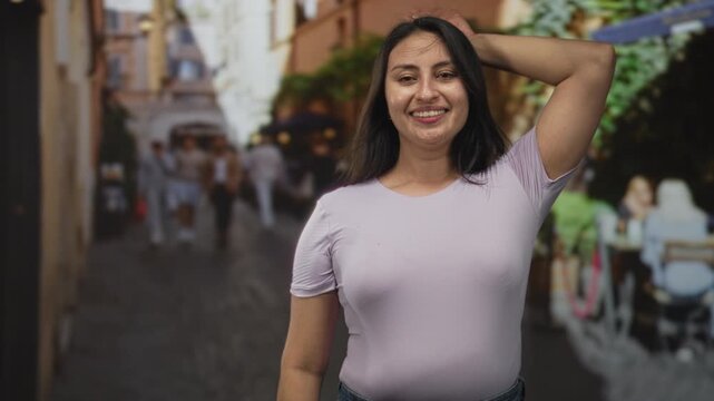 Woman smiling and waving hands in a narrow city street with cafe terraces and pedestrians; joy playful confidence.