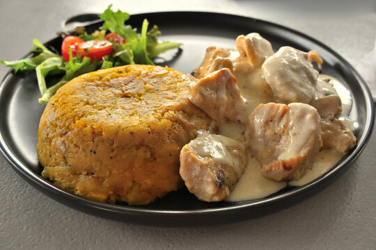 Mofongo con pollo en salsa de ajo cremosa acompa&ntilde;ado de ensalada fresca, servido en plato tradicional puertorrique&ntilde;o. 