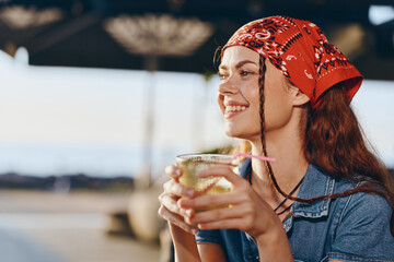 Lifestyle woman in modern boho-western denim street style enjoying a drink, smiling brightly with...