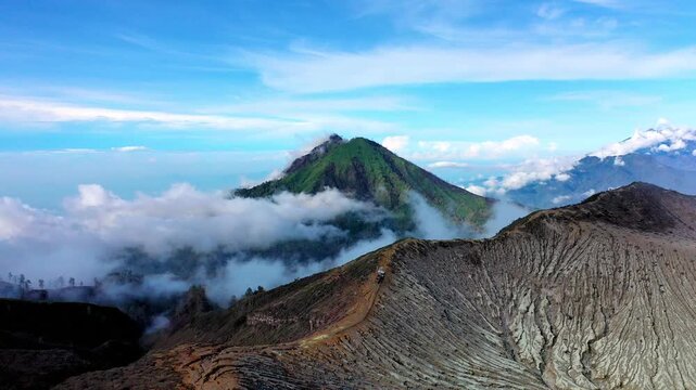 Aerial Panorama View of Volcano Crater Rim with Textured Grey Ash Slopes and Lush Green Mountain Peak Kawah Ijen. Horizon Rising Above White Clouds in East Java Indonesia. Wild Nature Landscape 4k
