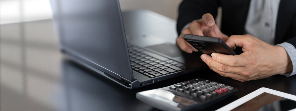 Businessman using smartphone with laptop and calculator for mobile finance and budgeting