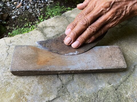Senior hands sharpening traditional knife on grinding stone. rural culture.