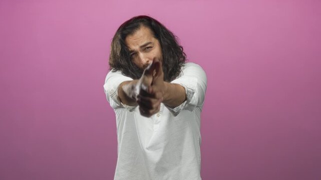 Man forming finger gun with both hands and direct gaze in pink studio closeup, wearing white shirt; focus determination.