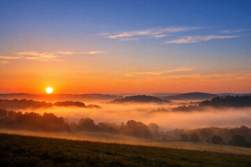 Fototapeta premium Golden sunrise over misty rolling hills and valleys, tranquil morning landscape with vibrant orange and blue sky, serene nature background