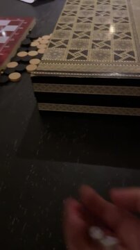 Close-up of a hand holding dice over an ornate backgammon board. Traditional handmade wooden game set in a luxury Egypt resort. Authentic Arabian leisure and table games. Cinematic atmosphere.