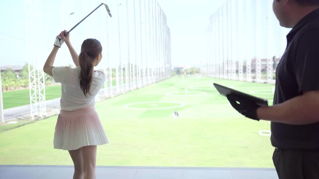 Golf instructor reviewing launch monitor swing data with female golfer at driving range