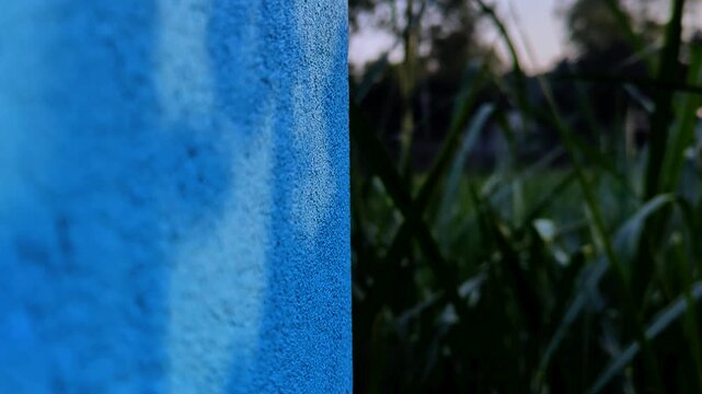 Blue textured wall next to lush green grass in a field.